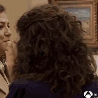 a woman with curly hair is talking to another woman while wearing a blue shirt .