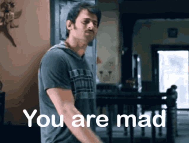 a man in a gray shirt is standing in front of a sign that says you are mad