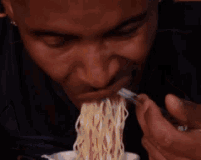 a man is eating noodles with a spoon and fork