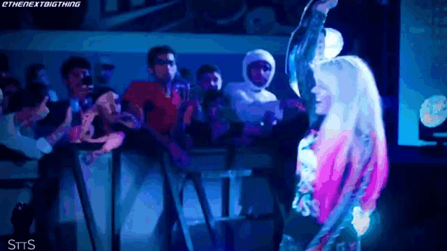 a woman in a pink and black outfit is standing in front of a crowd and a sign that says sits