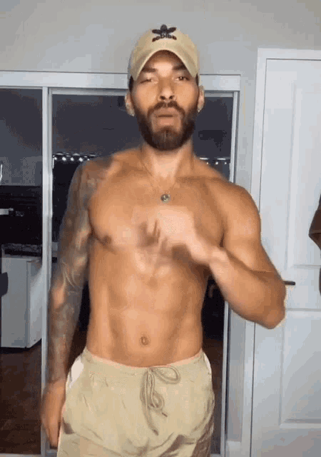 a shirtless man wearing a hat and shorts is standing in front of a sliding glass door .