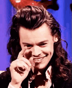 harry styles is smiling and pointing at the camera with his finger .