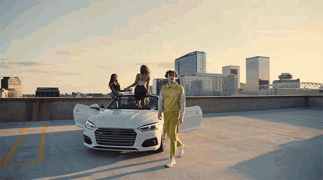 a man and two women are standing in front of a white car