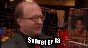 a man wearing glasses says " svaret er ja " in front of a display of shirts