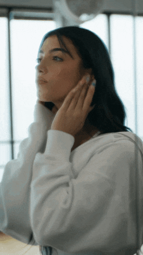 a woman in a white sweatshirt adjusts her hair