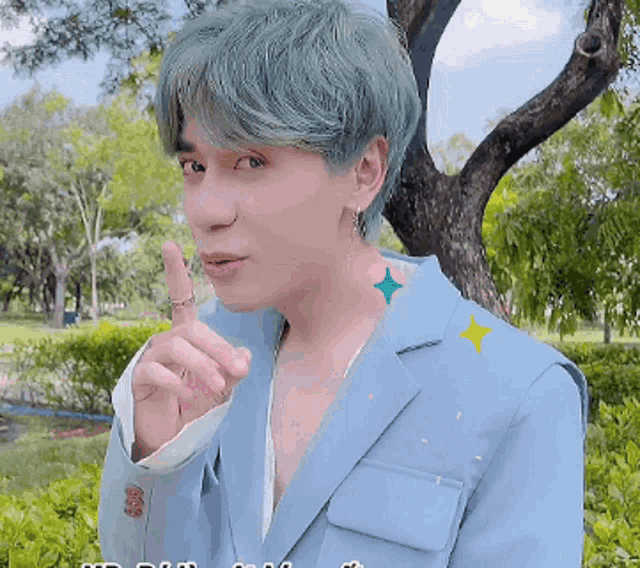 a man with green hair and a blue jacket is making a shhh gesture