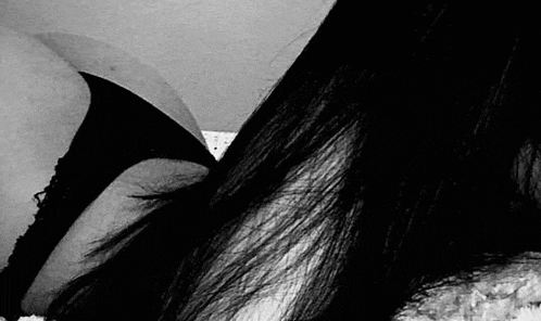 a black and white photo of a woman in a bra and panties laying on a bed .