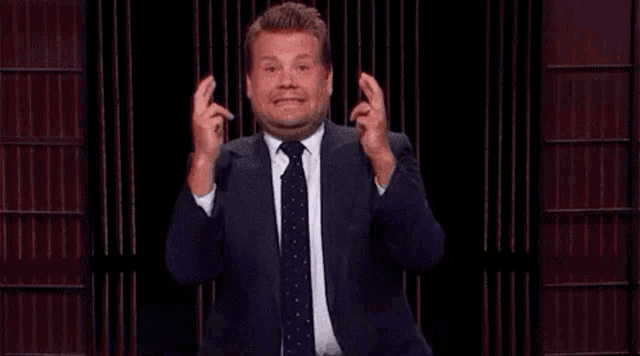 a man in a suit and tie is making a funny face while holding his fingers crossed .