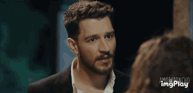 a man with a beard is looking at a woman in a suit and white shirt .