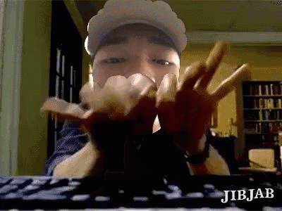 a man wearing a hat is making a peace sign with his hands while sitting in front of a keyboard .