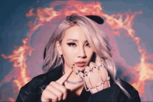 a woman with a lot of rings on her fingers is standing in front of a fire background