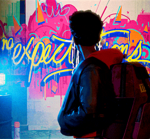 a man with a backpack stands in front of a wall that has graffiti on it that says no expectations