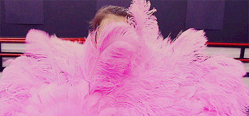 a man is wrapped in a pink feather boa covering his face .