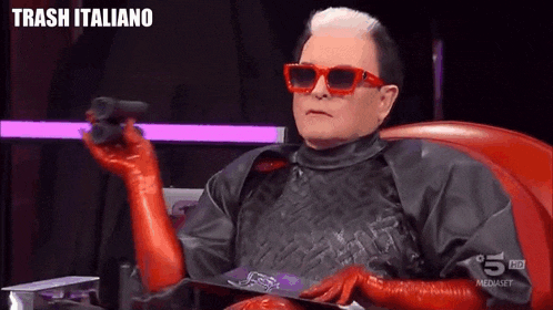 a man wearing red gloves and sunglasses is sitting in a chair with trash italiano written on the bottom