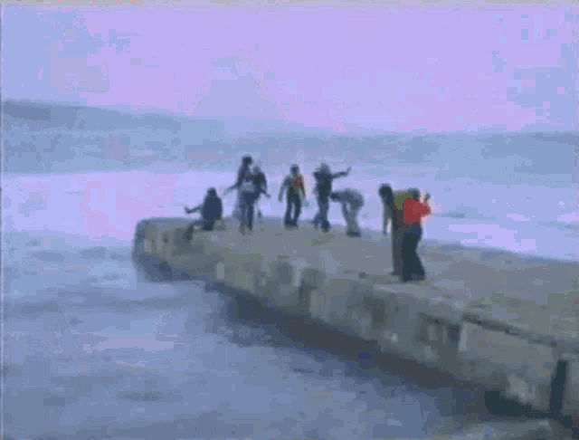 a group of people standing on a pier overlooking the ocean .