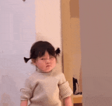 a little girl is standing in front of a door making a funny face .