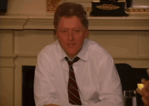 a man wearing a tie and a white shirt is sitting in front of a fireplace