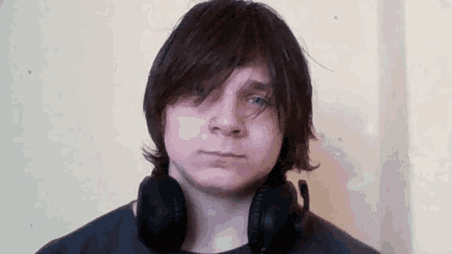 a young man wearing headphones and a black shirt looks at the camera .