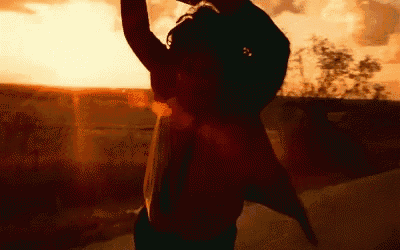 a person is standing in front of a sunset with their arms up in the air .