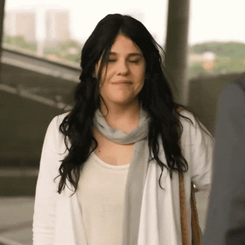 a woman wearing a white cardigan and a scarf looks down