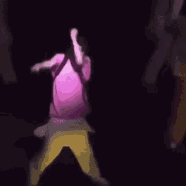 a man in a pink shirt and yellow pants is dancing on a stage with a microphone .