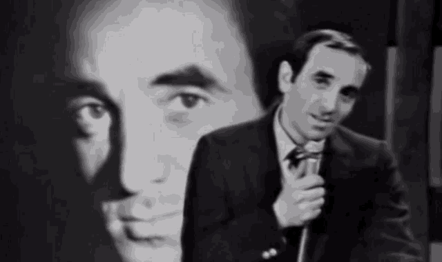 a man in a suit is holding a microphone in front of a picture of another man
