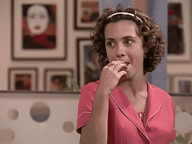 a woman in a pink shirt is biting her ring .