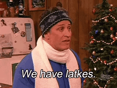 a man wearing a scarf and a hat is standing in front of a christmas tree .