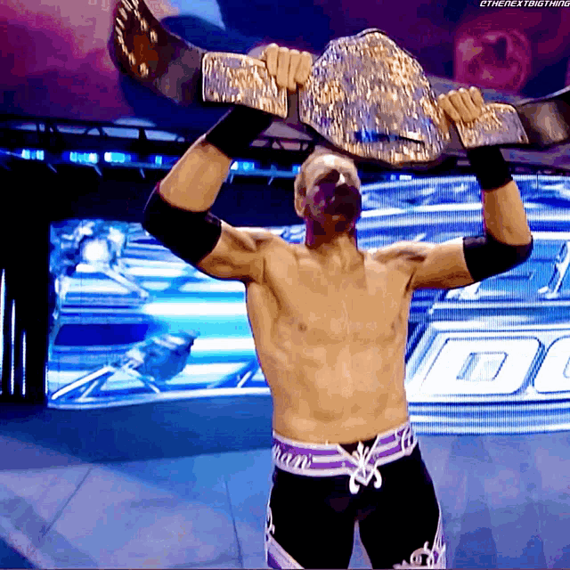 a shirtless wrestler is holding a wrestling belt over his head