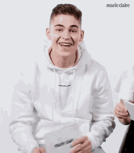 a young man in a white hoodie is laughing while holding a piece of paper .