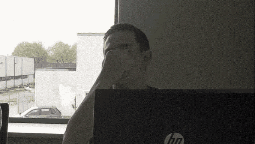 a man sitting in front of an hp laptop covering his face