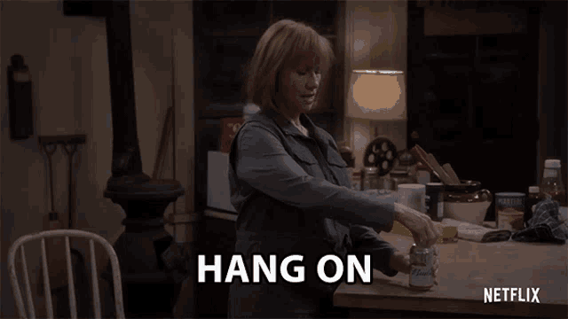 a woman is sitting at a table with a can of beer and the words hang on above her