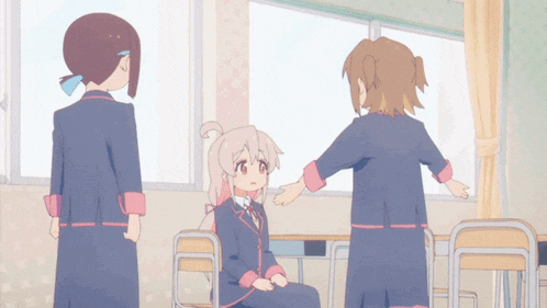 three anime girls are standing in a classroom and one of them is sitting at a desk