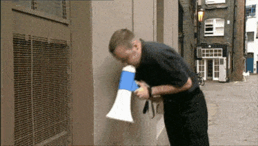 a man in a black shirt is blowing into a megaphone on a street