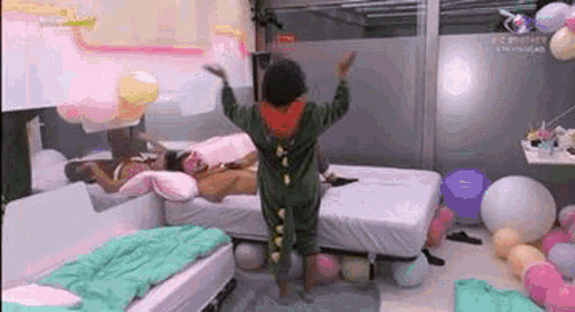 a person in a dinosaur costume is standing in a bedroom with balloons and a bed .