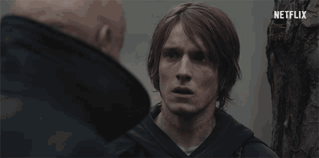 a man with a tattoo on his neck is talking to another man with a netflix logo in the background