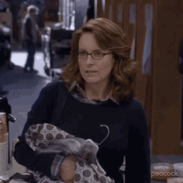 a woman wearing glasses is standing in a locker room holding a purse .