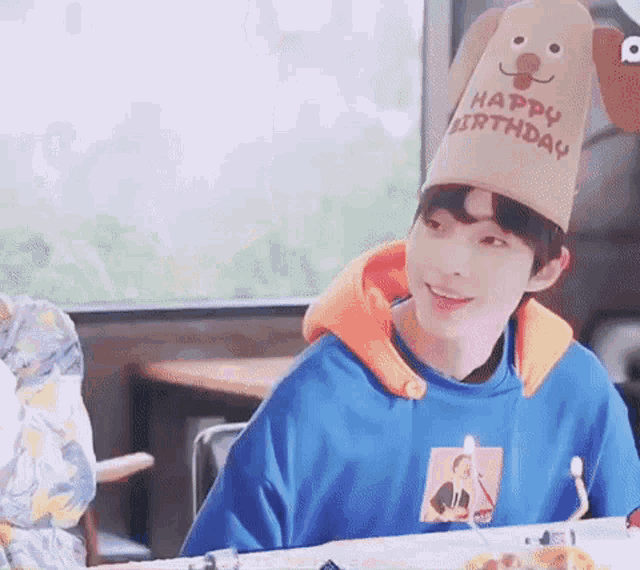 a young boy wearing a happy birthday hat is sitting at a table with a cake .