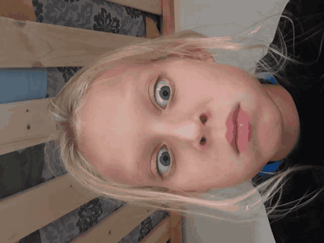 a young girl with blonde hair and blue eyes looks down at something