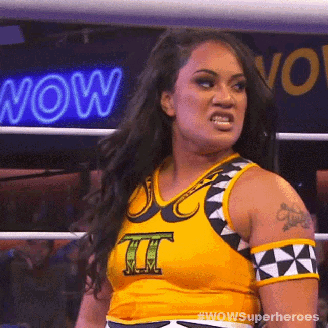 a woman in a wrestling ring wearing a yellow shirt with the letter t on it