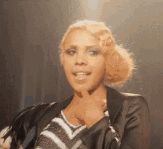 a woman with blonde hair and a black jacket is singing into a microphone .