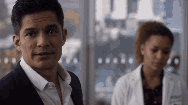a man in a suit and white shirt stands in front of a woman in a white lab coat