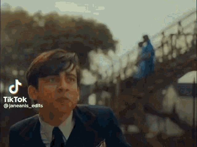 a man in a suit and tie is standing on a bridge with a woman in a blue dress in the background .