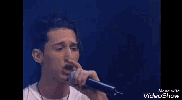 a young man is singing into a microphone while holding his nose .