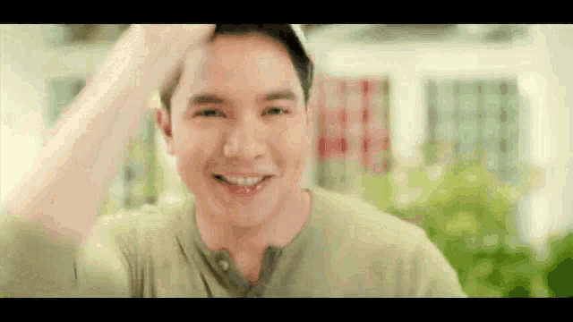 a man in a green shirt is smiling and holding his hand to his forehead .