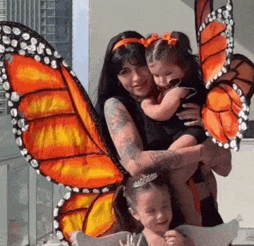 a woman is holding two little girls with butterfly wings