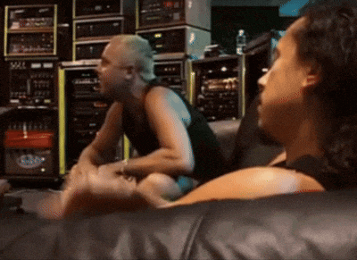 two men are sitting on a couch in a room with a stack of boxes behind them