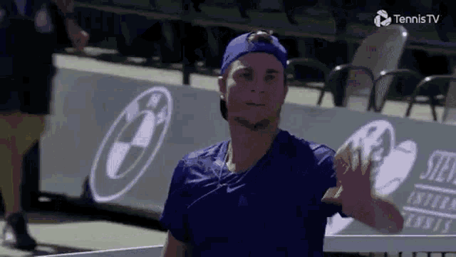 a tennis player wearing a blue hat is waving at the camera .
