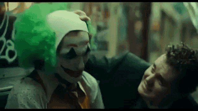 a man in a suit is touching the head of a clown in a green wig .