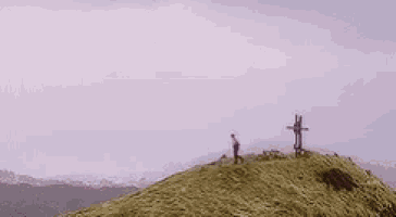 a person standing on top of a grassy hill with a cross on it